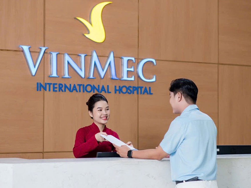 Receptionist in red traditional ao dai handing medical records to a visitor at Vinmec International Hospital