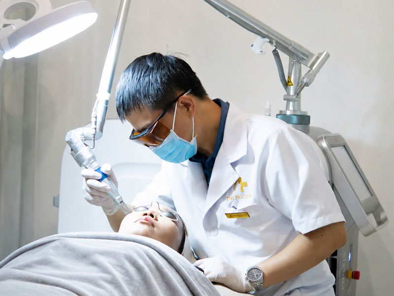 Doctor in a white coat wearing laser safety goggles treating a patient's facial skin. laser tattoo removal training near me in Hanoi